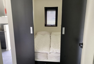 Kleine slaapkamer met bed, witte dekbedden en schuifdeuren in Modus lodge te Bad Hoophuizen, Nederland.