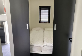Dormitorio pequeño con cama, edredones blancos y puertas corredizas en la cabaña Modus en Bad Hoophuizen.