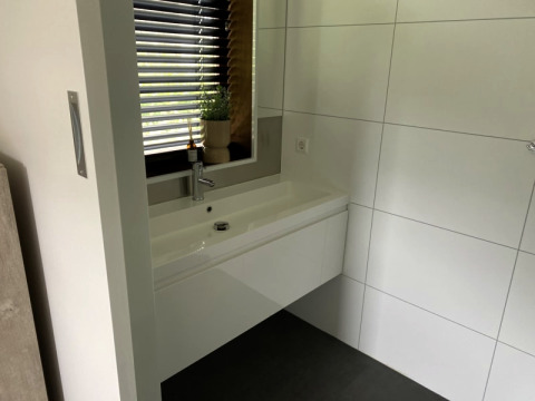 Lavabo de salle de bains moderne avec grand miroir, carrelage et fenêtre au Modus lodge à Bad Hoophuizen, Pays-Bas.