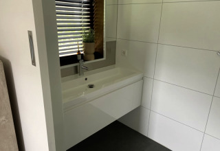 Lavabo de salle de bains moderne avec grand miroir, carrelage et fenêtre au Modus lodge à Bad Hoophuizen, Pays-Bas.