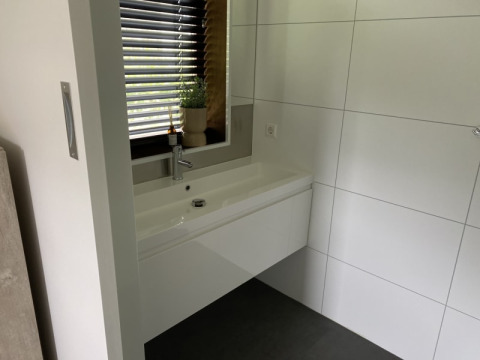 Lavabo de baño moderno con espejo grande, pared de baldosas y ventana en Modus lodge, Bad Hoophuizen, Países Bajos.