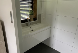 Lavabo da bagno moderno con grande specchio, parete piastrellata e finestra al lodge Modus, Bad Hoophuizen, Paesi Bassi.