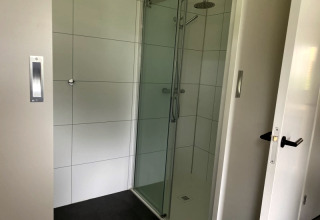 Douche moderne avec porte vitrée dans un lodge à Modus, Bad Hoophuizen, Pays-Bas, aux carreaux blancs.