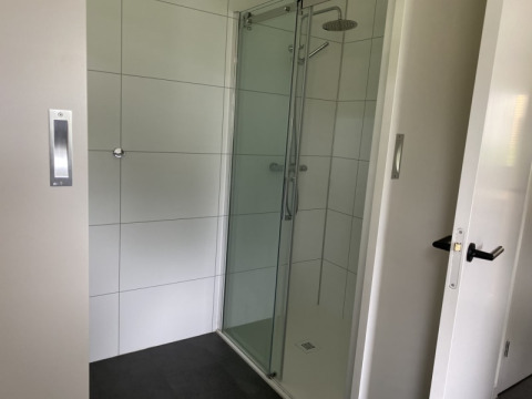 Moderne douche met glazen deur in een lodge bij Modus, Bad Hoophuizen, Nederland, met witte tegels.