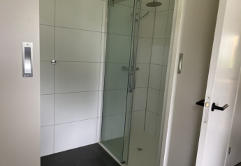 Ducha moderna con puerta de cristal en una cabaña en Modus, Bad Hoophuizen, Países Bajos, y azulejos blancos.