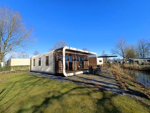 Lodge Modus moderne à Bad Hoophuizen, Pays-Bas, avec terrasse et vue sur l'eau lors d'une journée ensoleillée.