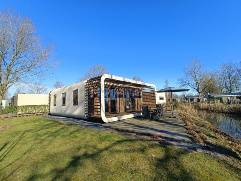 Moderne Modus-lodge bij Bad Hoophuizen in Nederland met terras en uitzicht op het water op een zonnige dag.