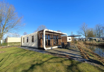 Moderne Modus-lodge bij Bad Hoophuizen in Nederland met terras en uitzicht op het water op een zonnige dag.