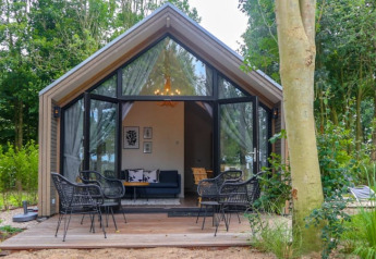 Beach House lodge met glazen deuren, terras met stoelen, gelegen in een groene, bosrijke omgeving.