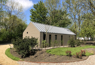 Strandhuis bij Bad Hoophuizen in Nederland, omgeven door tuin, begroeiing en hoge bomen op een zonnige dag.