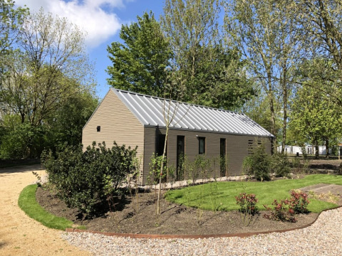 Casa sulla spiaggia a Bad Hoophuizen, Paesi Bassi, circondata da alberi, giardino e cielo sereno e soleggiato.