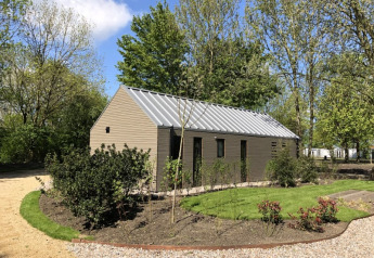 Strandhus ved Bad Hoophuizen i Holland, omgivet af grønt og træer under en blå himmel med solskin.