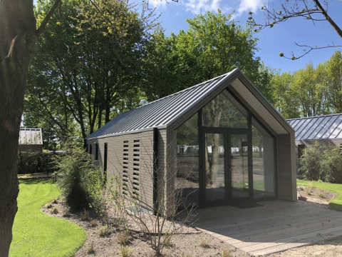 Moderne træhytte med store glaspartier ved Beach House, Bad Hoophuizen, Holland omgivet af grøn natur.