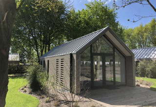 Moderne træhytte med store glaspartier ved Beach House, Bad Hoophuizen, Holland omgivet af grøn natur.