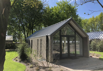 Moderne træhytte med store glaspartier ved Beach House, Bad Hoophuizen, Holland omgivet af grøn natur.