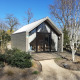 Et lille strandhus-lodge med moderne design, omgivet af natur og træer under en blå himmel.