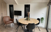 Eethoek in Tiny Beach House bij Bad Hoophuizen met ronde houten tafel, zwarte stoelen en kamerplanten.