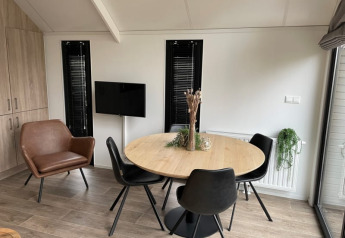 Eethoek in Tiny Beach House bij Bad Hoophuizen met ronde houten tafel, zwarte stoelen en kamerplanten.