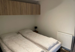 Dos camas individuales con ropa de cama blanca en un dormitorio minimalista en Tiny Beach House, Bad Hoophuizen, Países Bajos.