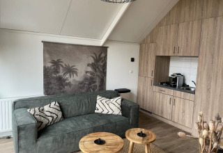 Sala moderna en Tiny Beach House, Bad Hoophuizen, Países Bajos, con sofá verde y cocina compacta.