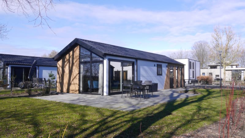 Lodge Velthorst moderno con grandes ventanales, muebles de terraza y jardín bajo un cielo despejado.