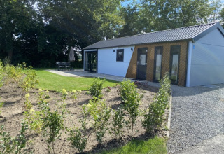 Moderne lodge Velthorst ved Bad Hoophuizen i Holland med have, terrasse og omgivet af grønne træer.