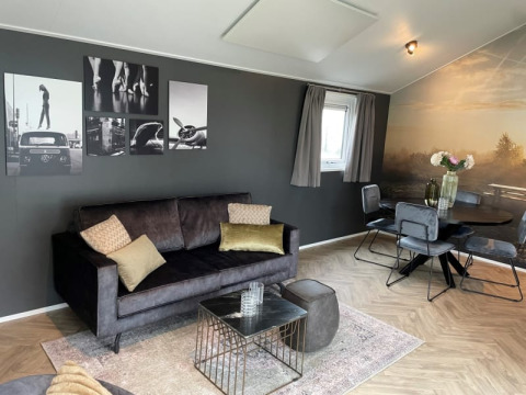 Stilfuld stue i Velthorst-lodge på Bad Hoophuizen, Holland, med sofa, moderne kunst og spiseområde.