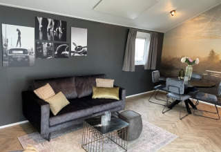 Stilfuld stue i Velthorst-lodge på Bad Hoophuizen, Holland, med sofa, moderne kunst og spiseområde.