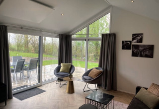 Salon moderne lodge Velthorst à Bad Hoophuizen avec grandes fenêtres donnant sur terrasse et jardin verdoyant.