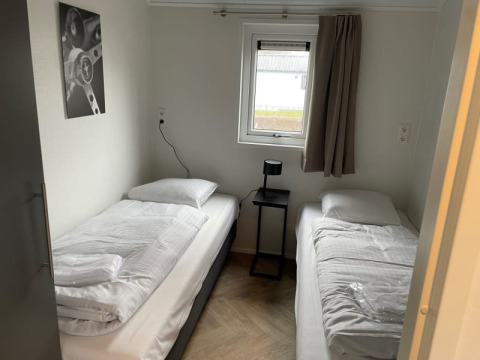 Habitación sencilla con dos camas individuales, mesa negra pequeña, ventana y cortina en Velthorst, Bad Hoophuizen.