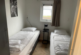 Habitación sencilla con dos camas individuales, mesa negra pequeña, ventana y cortina en Velthorst, Bad Hoophuizen.