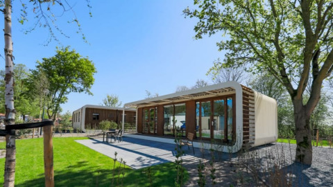 Moderne Modus Wellness-Lodge mit Glasfront in grüner Natur, umgeben von Bäumen und gepflegtem Rasen.