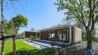 Moderna cabaña Modus Wellness con grandes ventanales de cristal, rodeada de césped y árboles frondosos.