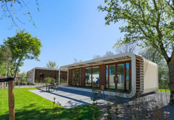 Modern Modus Wellness lodge with large glass windows, surrounded by green lawn and leafy trees in nature.