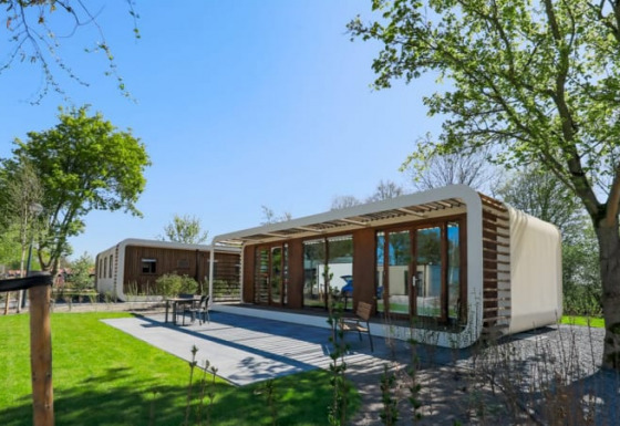 Moderna cabaña Modus Wellness con grandes ventanales de cristal, rodeada de césped y árboles frondosos.