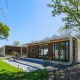 Moderne Modus Wellness-lodge med glasfacade midt i naturen, omgivet af grønne træer og græsplæne.