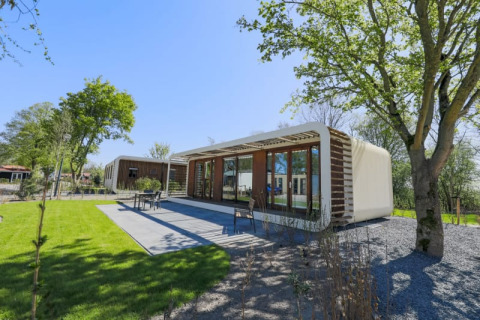 Moderne Lodge bei Modus Wellness in Bad Hoophuizen, Niederlande, mit Terrasse, Bäumen und grüner Rasenfläche.