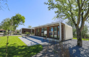 Lodge moderno en Modus Wellness, Bad Hoophuizen, Países Bajos, rodeado de césped verde, árboles y terraza.