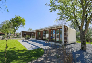 Lodge moderno en Modus Wellness, Bad Hoophuizen, Países Bajos, rodeado de césped verde, árboles y terraza.