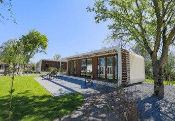 Modern lodge at Modus Wellness, Bad Hoophuizen, Netherlands, surrounded by green grass, trees and a patio area.