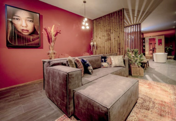 Stilfuld lounge med moderne sofa, rød væg, kunstværk og wellness-område i Modus Wellness, Bad Hoophuizen.
