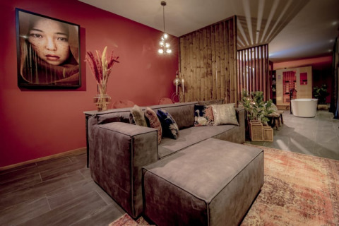 Zona lounge elegante da Modus Wellness a Bad Hoophuizen, con divano moderno, parete rossa e area benessere.