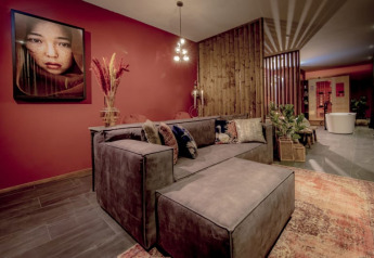 Stylish lounge at Modus Wellness, Bad Hoophuizen, with modern sofa, red wall, artwork, and a wellness area.