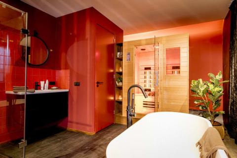 Modernes Badezimmer mit Sauna, freistehender Badewanne, roten Wänden und Pflanze im Modus Wellness, Bad Hoophuizen.