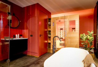 Baño moderno con sauna, bañera exenta, paredes rojas y planta en Modus Wellness, Bad Hoophuizen, Países Bajos.