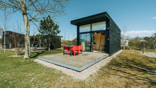 Casa pequeña moderna negra con terraza de madera y grandes ventanales en De Klepperstee, Países Bajos.