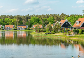 Vakantiepark met glampingaccommodaties aan een rustig meer, omgeven door bomen en vakantiehuisjes.