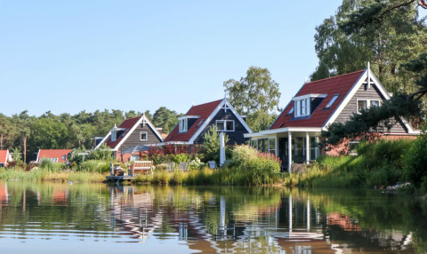 Vakantiepark met luxe glamping accommodaties langs een rustig meer, met charmante huisjes en natuur.