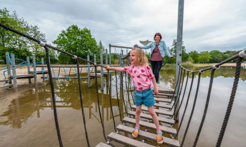 Moeder en dochter genieten van een avontuurlijke dag op een touwbrug bij een vakantiepark met glamping.