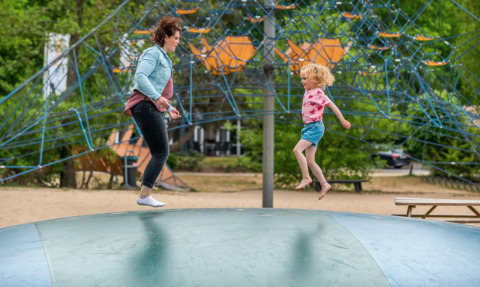Volwassene en kind springen samen op een luchtkussen bij een vakantiepark met glamping accommodatie.